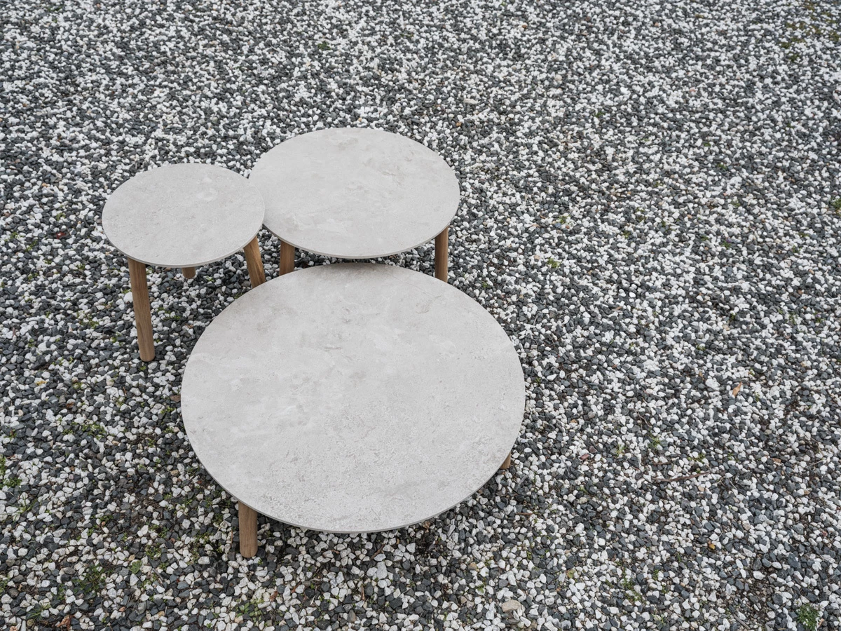 Lento coffee tables and side table by Vincent Sheppard, featuring Sabbia Panna stone tops and solid teak legs, set on a bed of white and grey gravel.